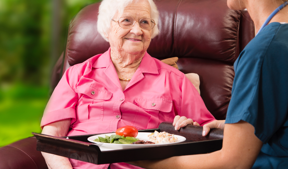 Caregiver handing a senior a tray with her meal on it
