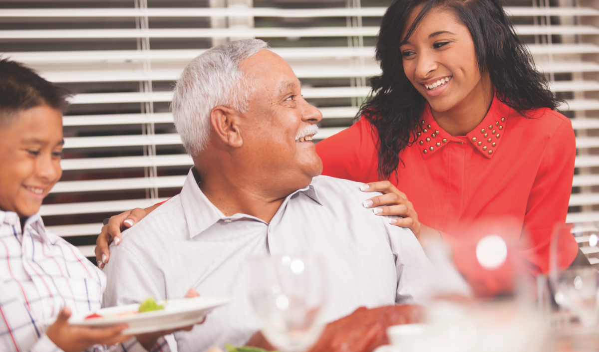 Two pre-teens smiling and having dinner with their grandfather